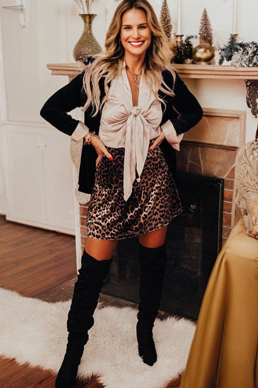 Model wearing Leopard Tiered Patchwork Mini Skirt from a women's boutique, styled with a chic blouse and over-the-knee boots.