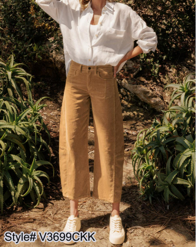 Trendy women's clothing featuring a stylish casual outfit with wide-leg pants and a chic white shirt in a natural setting.