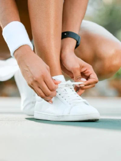 Close-up of a person tying laces on trendy white sneakers, perfect for casual women's fashion and stylish everyday wear.